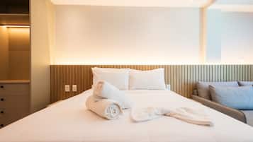 A hotel room with a neatly made bed, a wooden headboard, and a seating area with a chair and a small table.