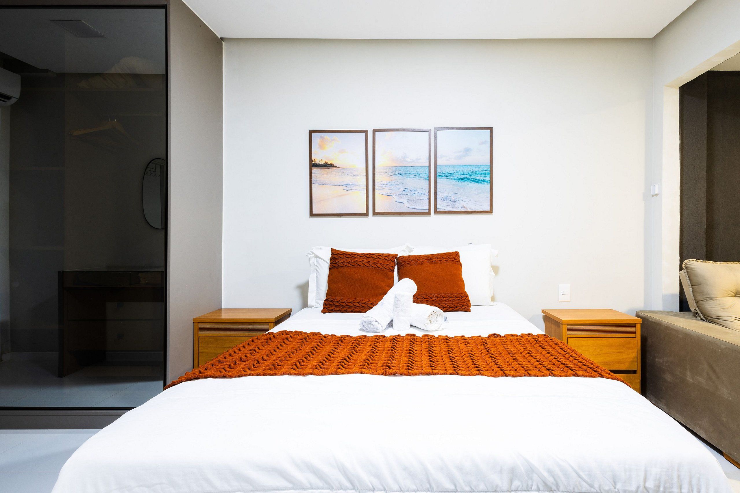 Une chambre d’hôtel moderne avec un grand lit, une table de chevet en bois, une cabine de douche en verre et une vue sur l’océan.