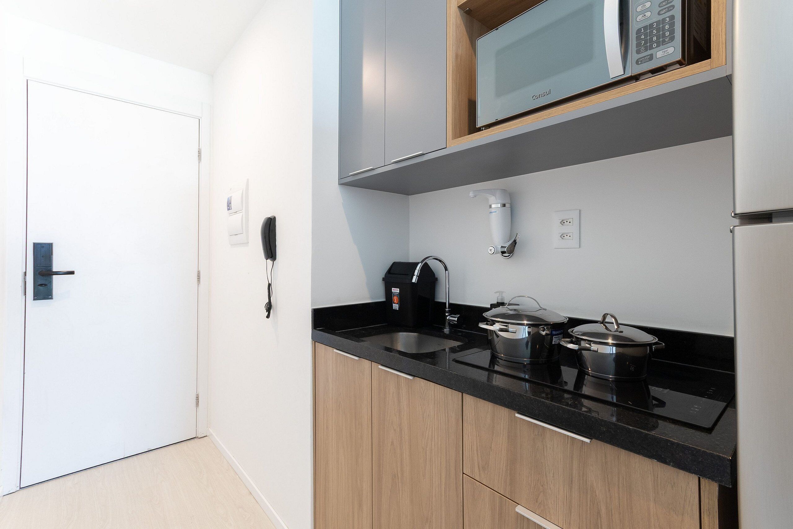 A modern kitchen with a black countertop, wooden cabinets, a microwave, a coffee maker, and a kettle.