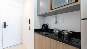 A modern kitchen with a black countertop, wooden cabinets, a microwave, a coffee maker, and a kettle. - Art Studio Housi Salvador by Carpediem (Salvador)