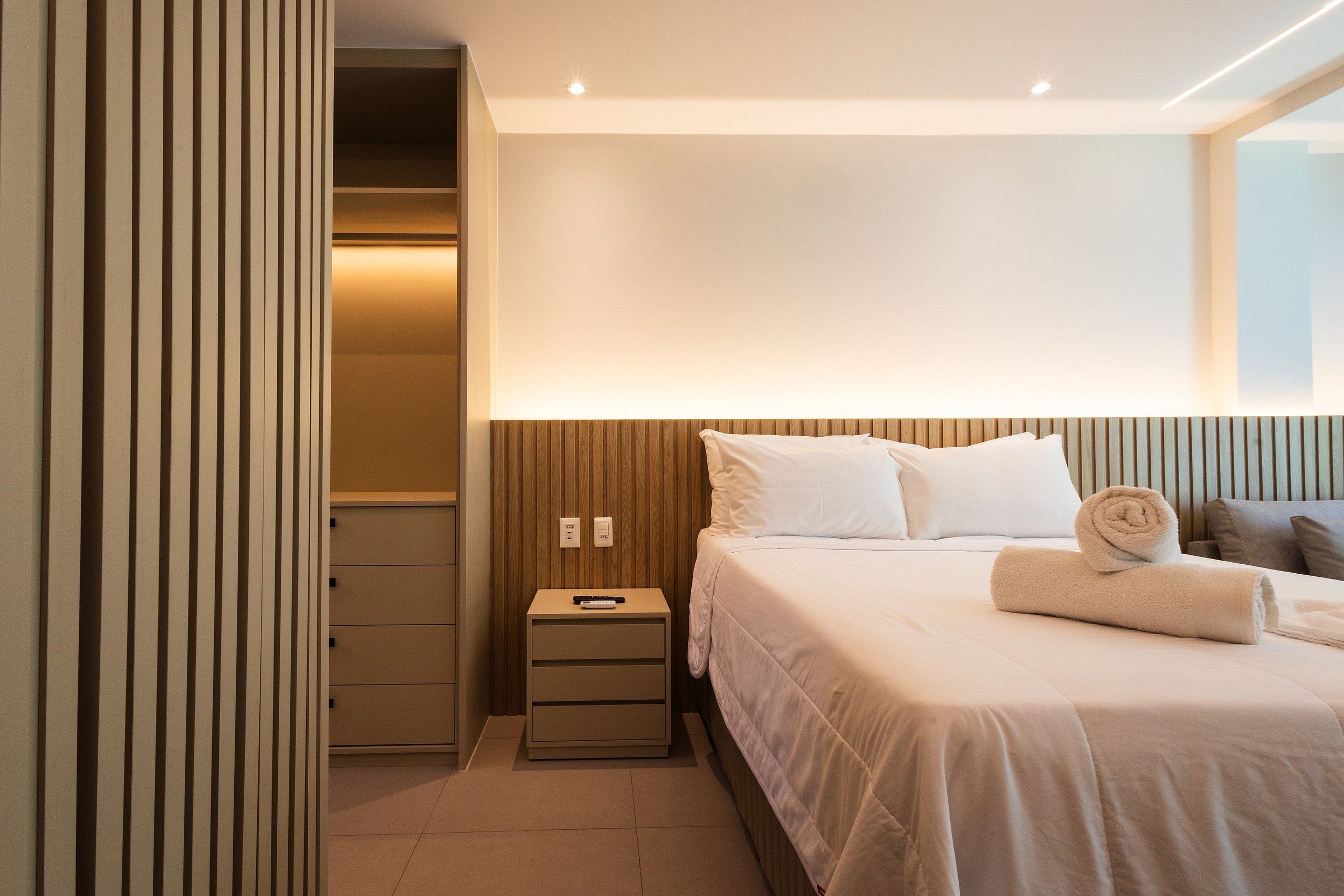 Ein Hotelzimmer mit einem ordentlich bezogenen Bett, einem Nachttisch mit Fernbedienung und einer Wandleuchte.