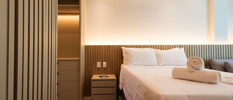 Ein Hotelzimmer mit einem ordentlich bezogenen Bett, einem Nachttisch mit Fernbedienung und einer Wandleuchte.