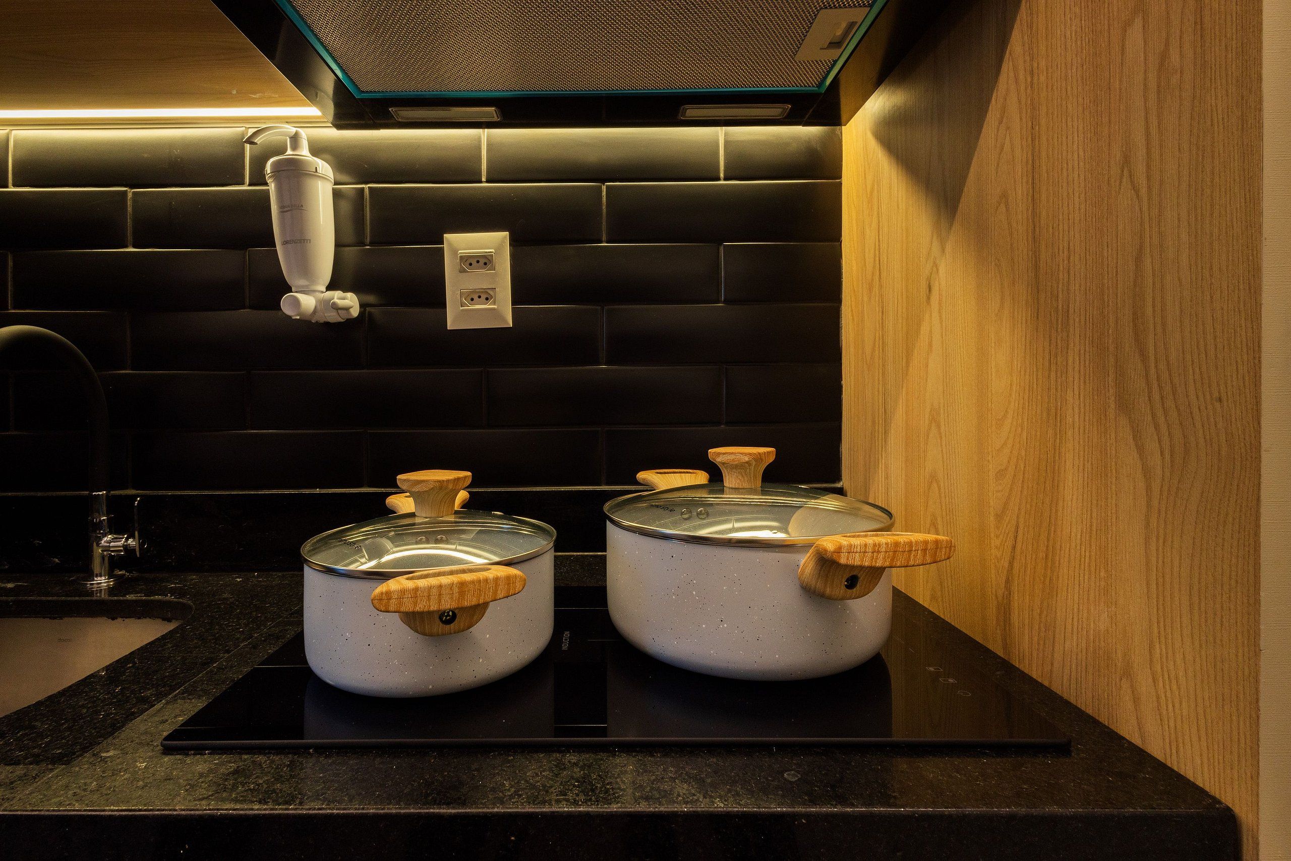 A kitchen with two pots on a black countertop, a black tiled backsplash, and a wooden wall.