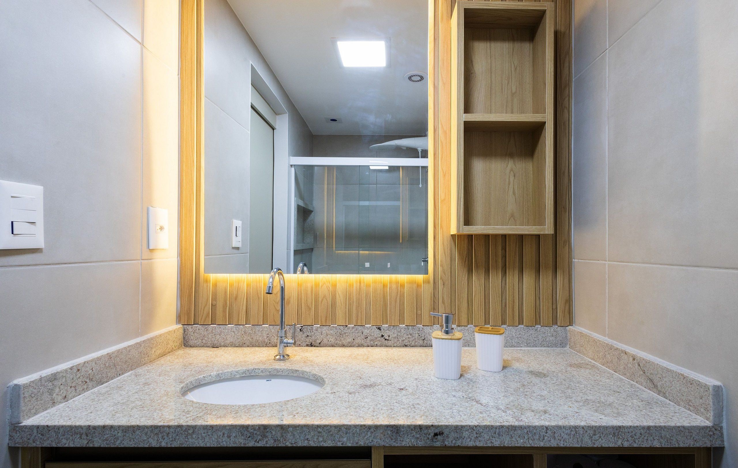 Un bagno moderno con un piano in granito, un lavandino, uno specchio e scaffali in legno.