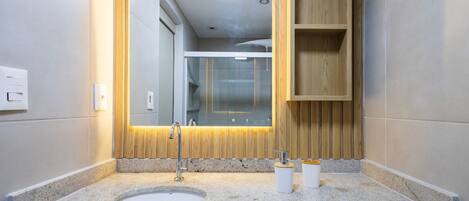 Un bagno moderno con un piano in granito, un lavandino, uno specchio e scaffali in legno.