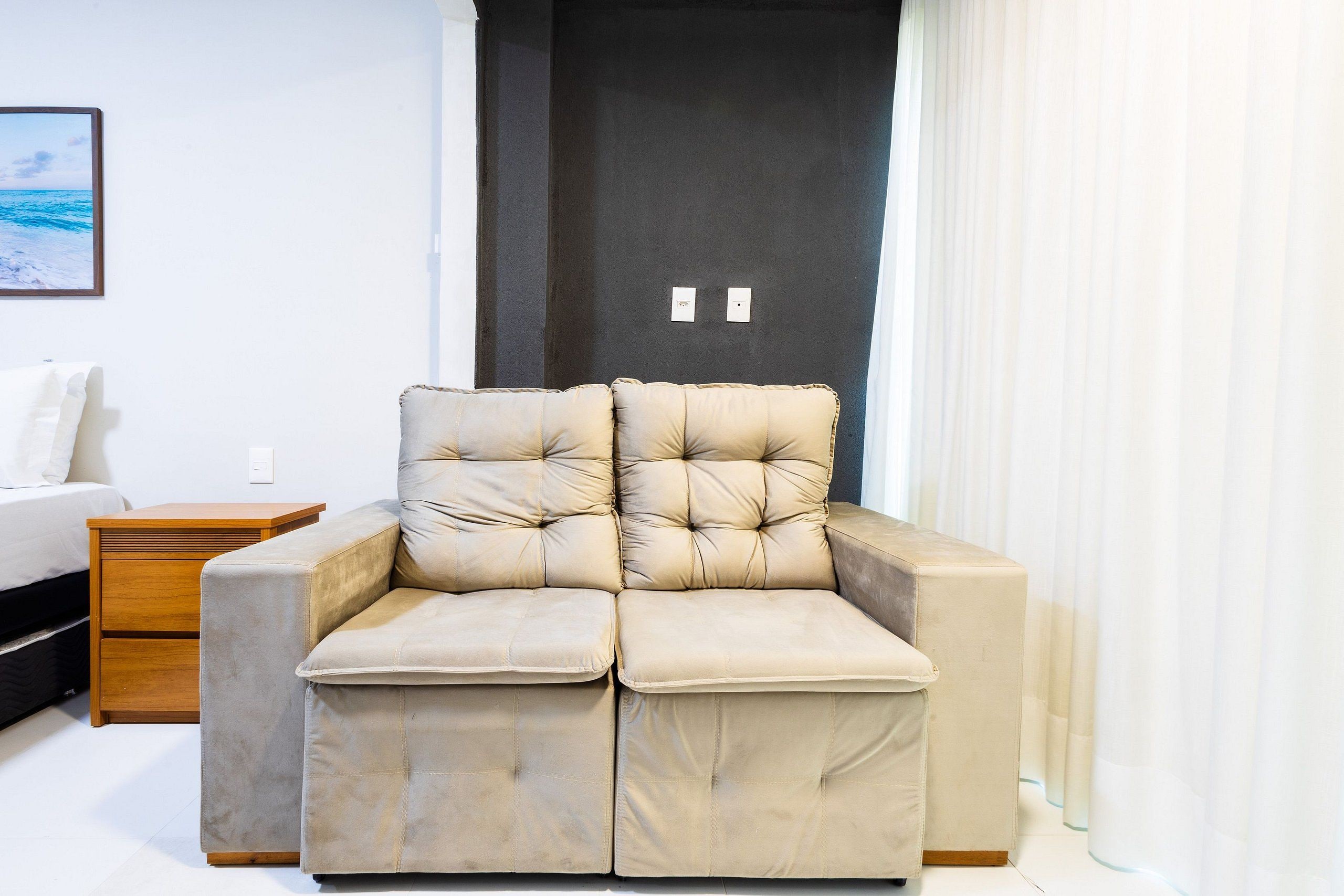 Una habitación moderna con un sofá color crema, una mesita de noche de madera y una cama.