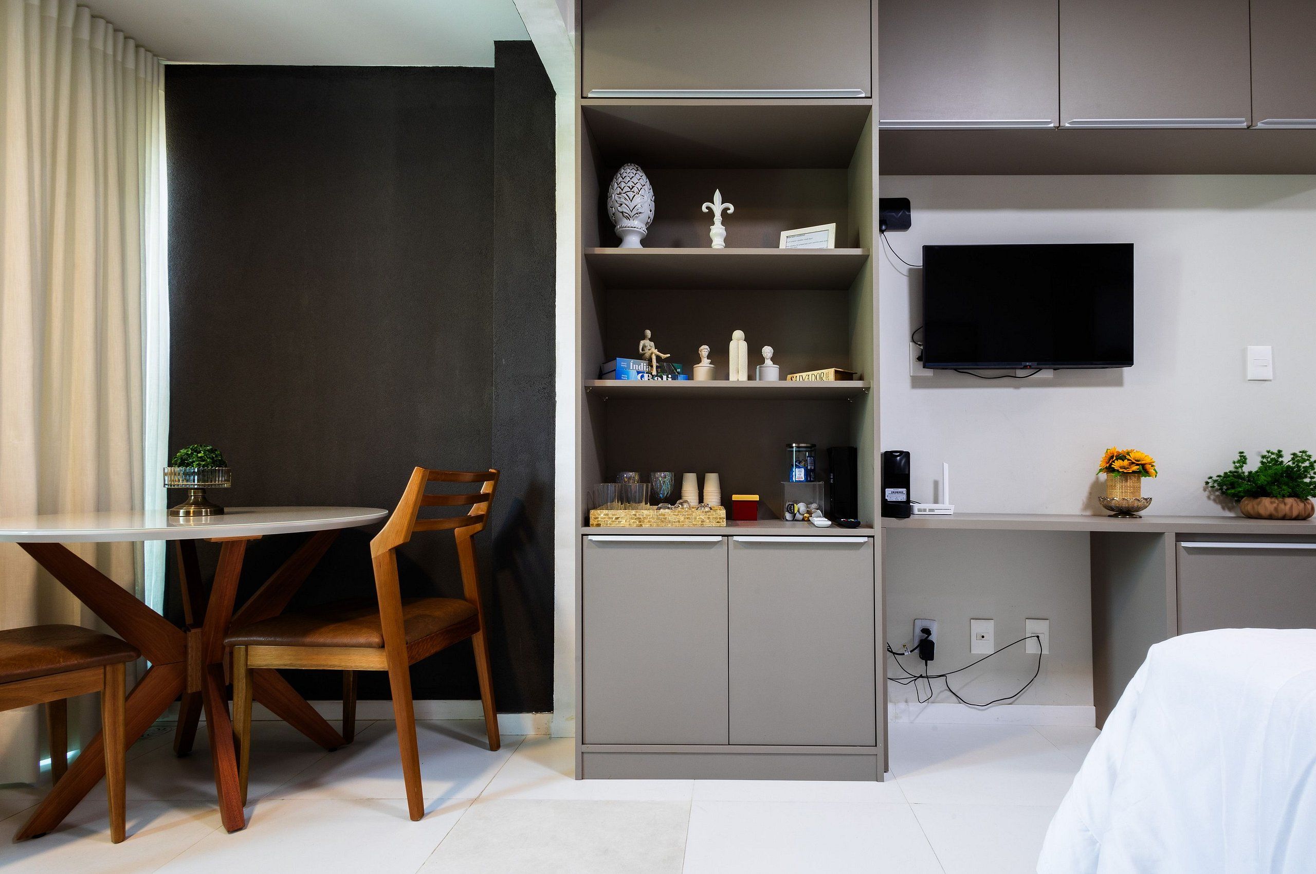 Een moderne hotelkamer met een zithoek, een grijs kastje met decoratieve objecten, een flatscreen televisie en een bed.