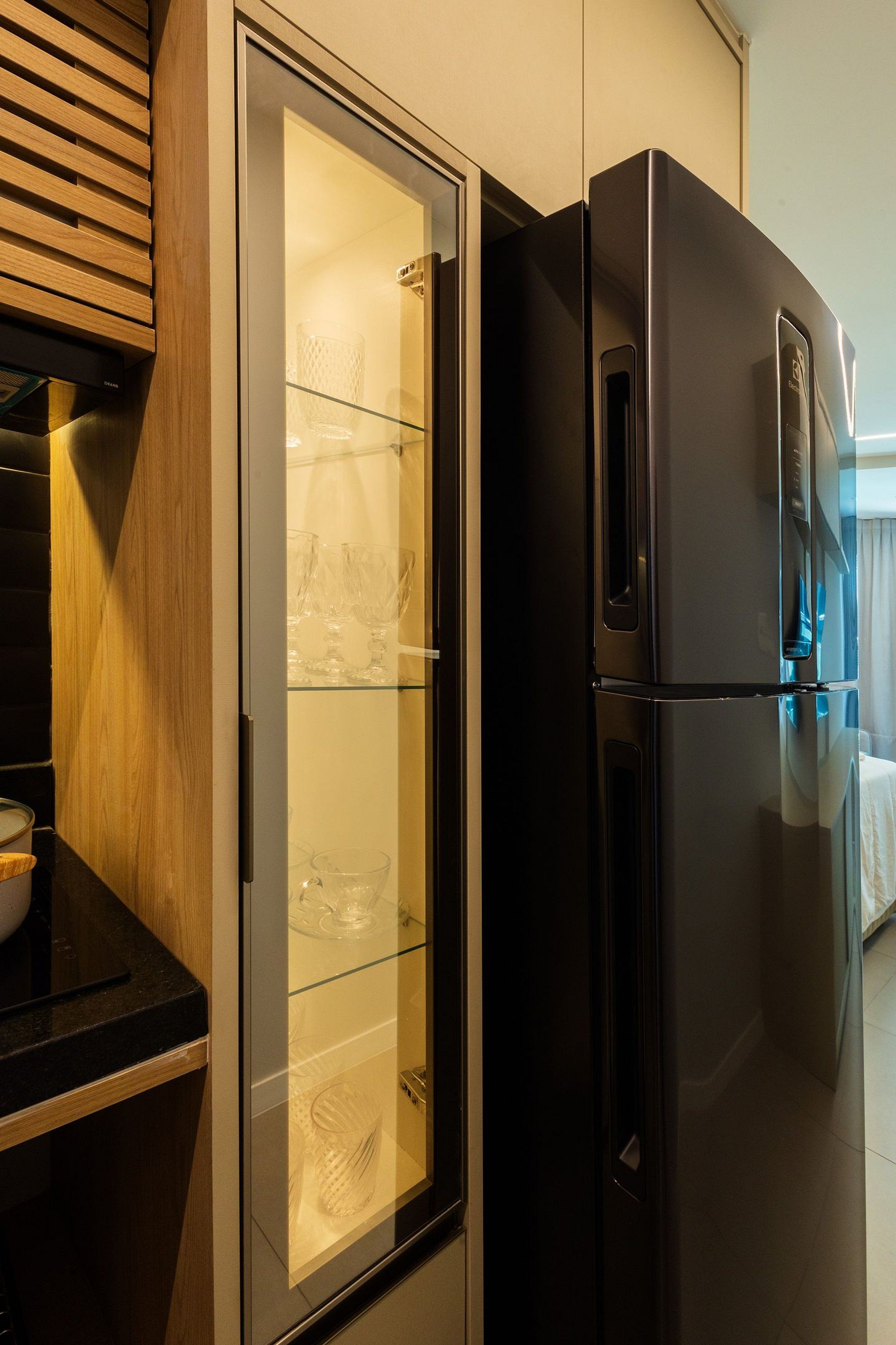 A modern kitchen with a black refrigerator, a glass-fronted cabinet, and wooden cabinetry.