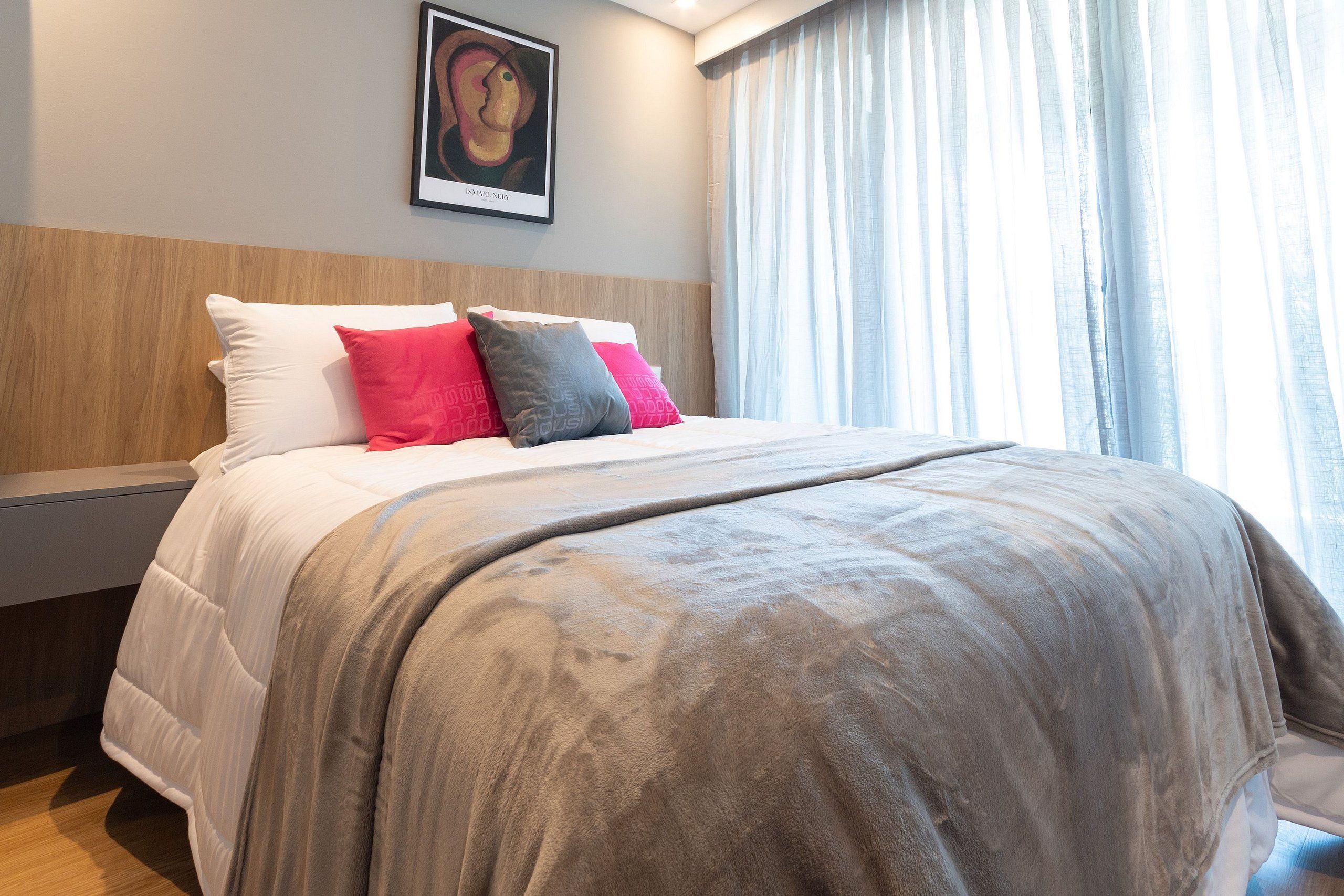 A neatly made bed with a grey blanket and pillows in red and grey.