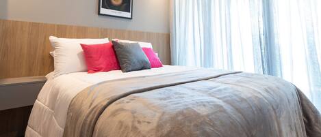 Una cama bien hecha con una manta gris y almohadas en rojo y gris.