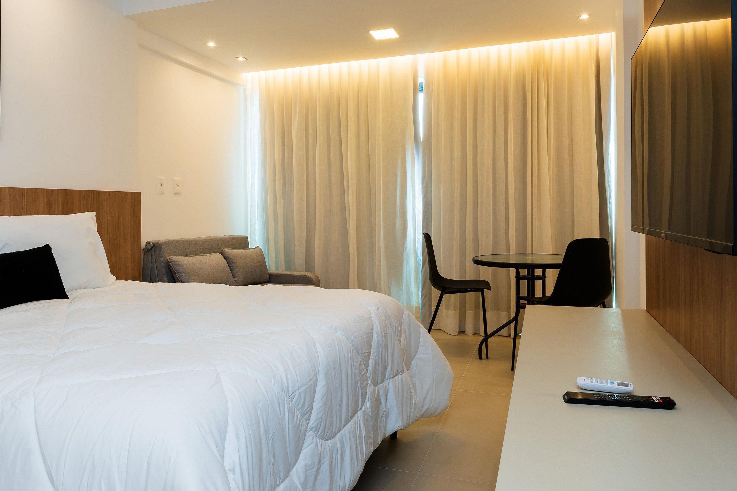 Quarto de hotel com uma cama grande, uma escrivaninha, uma cadeira e uma televisão.