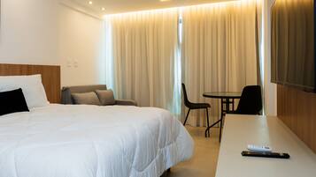 Quarto de hotel com uma cama grande, uma escrivaninha, uma cadeira e uma televisão.