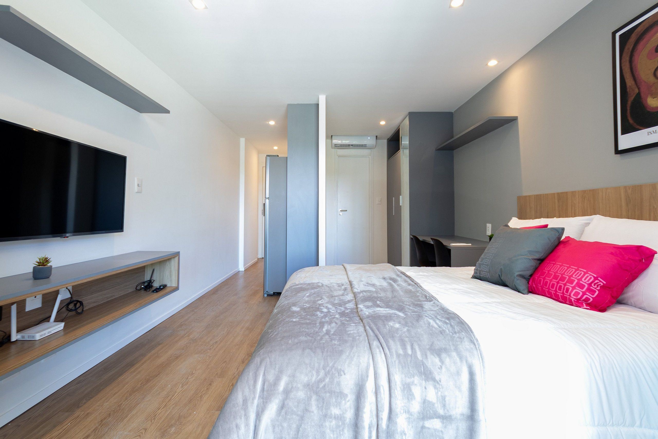 A modern bedroom with a large bed, a flat-screen TV mounted on the wall, and a built-in bench with storage.