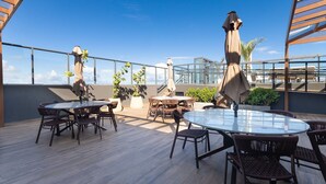 En udendørs terrasse med runde borde og stole, plantekrukker og parasoller.