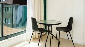 A modern room with a glass table and two chairs, a large window with curtains, and a view of a building outside.