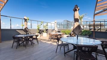 Eine Terrasse im Freien mit runden Tischen und Stühlen, Topfpflanzen und Sonnenschirmen.