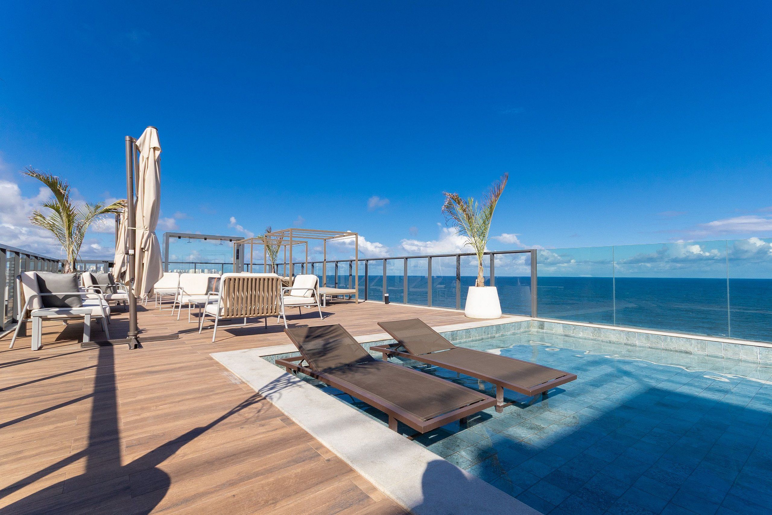 Um terraço com espreguiçadeiras, piscina e vista para o oceano.