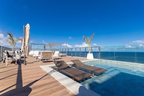A sun deck with lounge chairs, a pool, and a view of the ocean. - Art Studio Housi Salvador by Carpediem (Salvador)