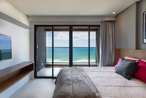 A bedroom with a large bed, a TV on the left, and a view of the ocean through a sliding door. - Art Studio Housi Salvador by Carpediem (Salvador)