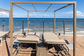 A deck with sun loungers and a glass railing overlooking the sea. - Art Studio Housi Salvador by Carpediem (Salvador)