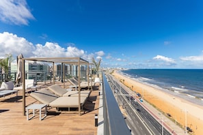 A rooftop lounge with sun loungers and a view of the beach and ocean. - Art Studio Housi Salvador by Carpediem (Salvador)