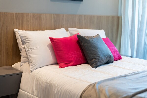 A neatly made bed with white and pink pillows, a wooden headboard, and a grey nightstand. - Art Studio Housi Salvador by Carpediem (Salvador)