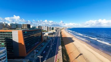 A coastal cityscape with a wide beach, modern buildings, and a clear blue sky.