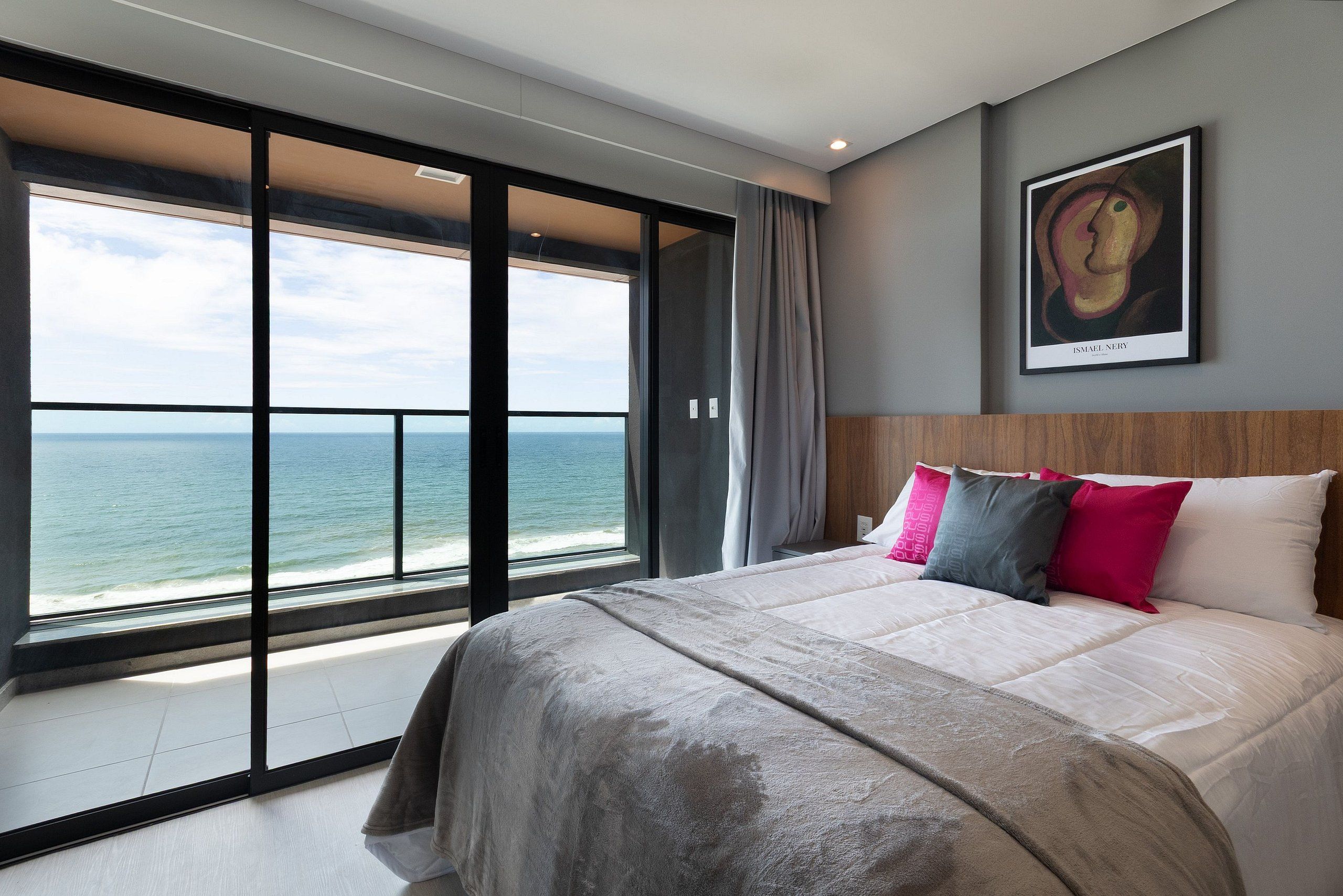Ein modernes Schlafzimmer mit einem großen Bett, Blick aufs Meer und einem gerahmten Kunstwerk an der Wand.