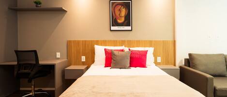 A hotel room with a bed, a desk, a chair, and a couch.