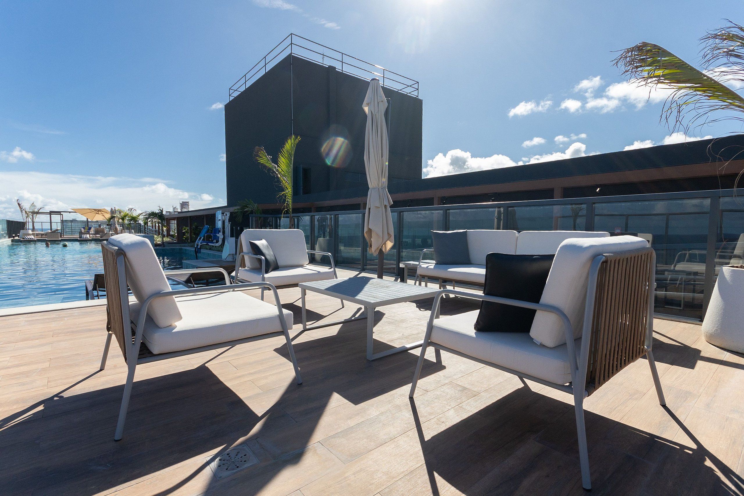 A rooftop pool area with white lounge chairs, a table, and an umbrella.