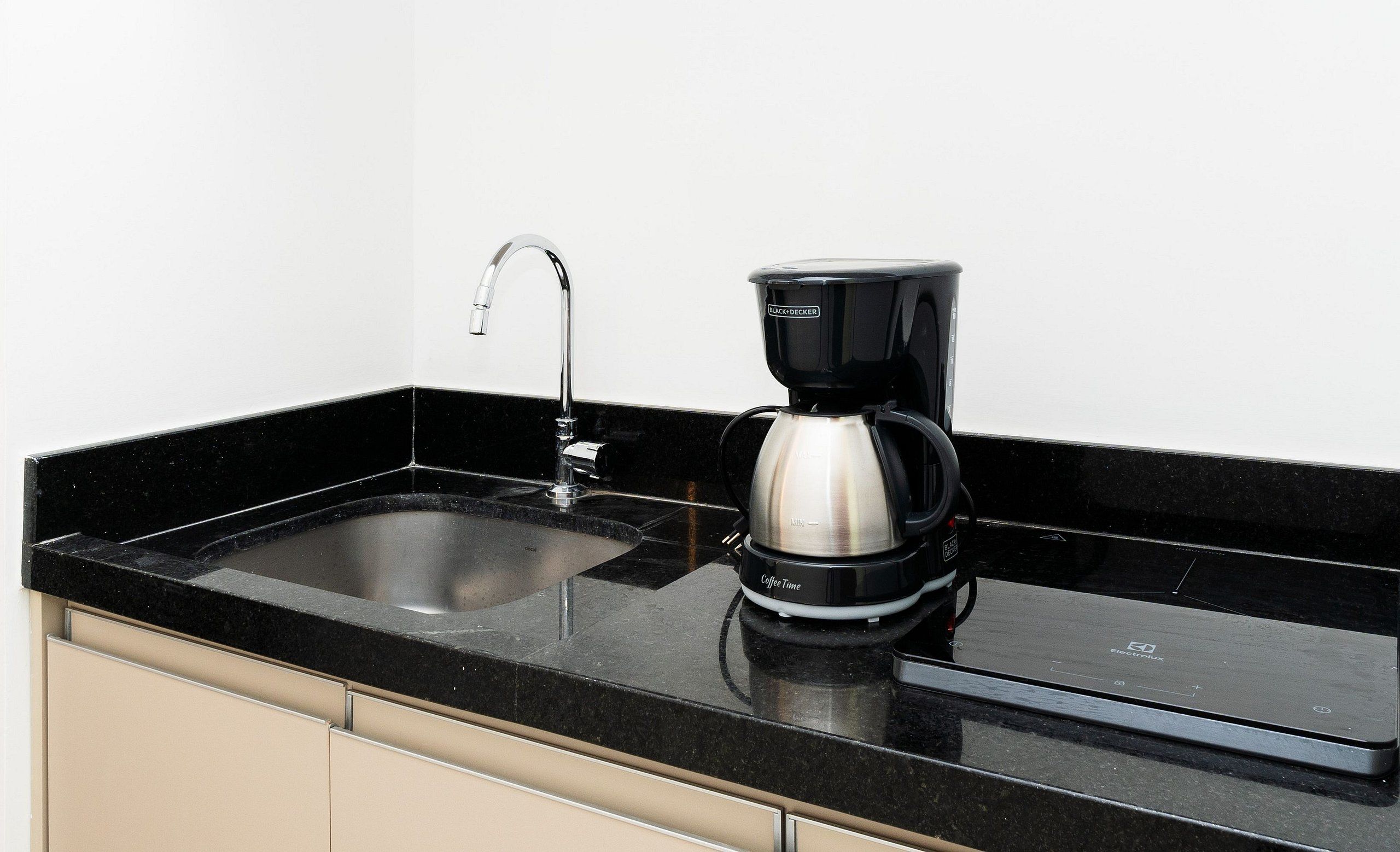 A kitchen with a black countertop, a stainless steel sink, and a black coffee maker.