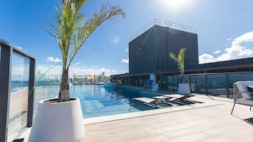 Ein Pool auf dem Dach mit Blick auf den Ozean, eine große Kübelpflanze und moderne Outdoor-Möbel.