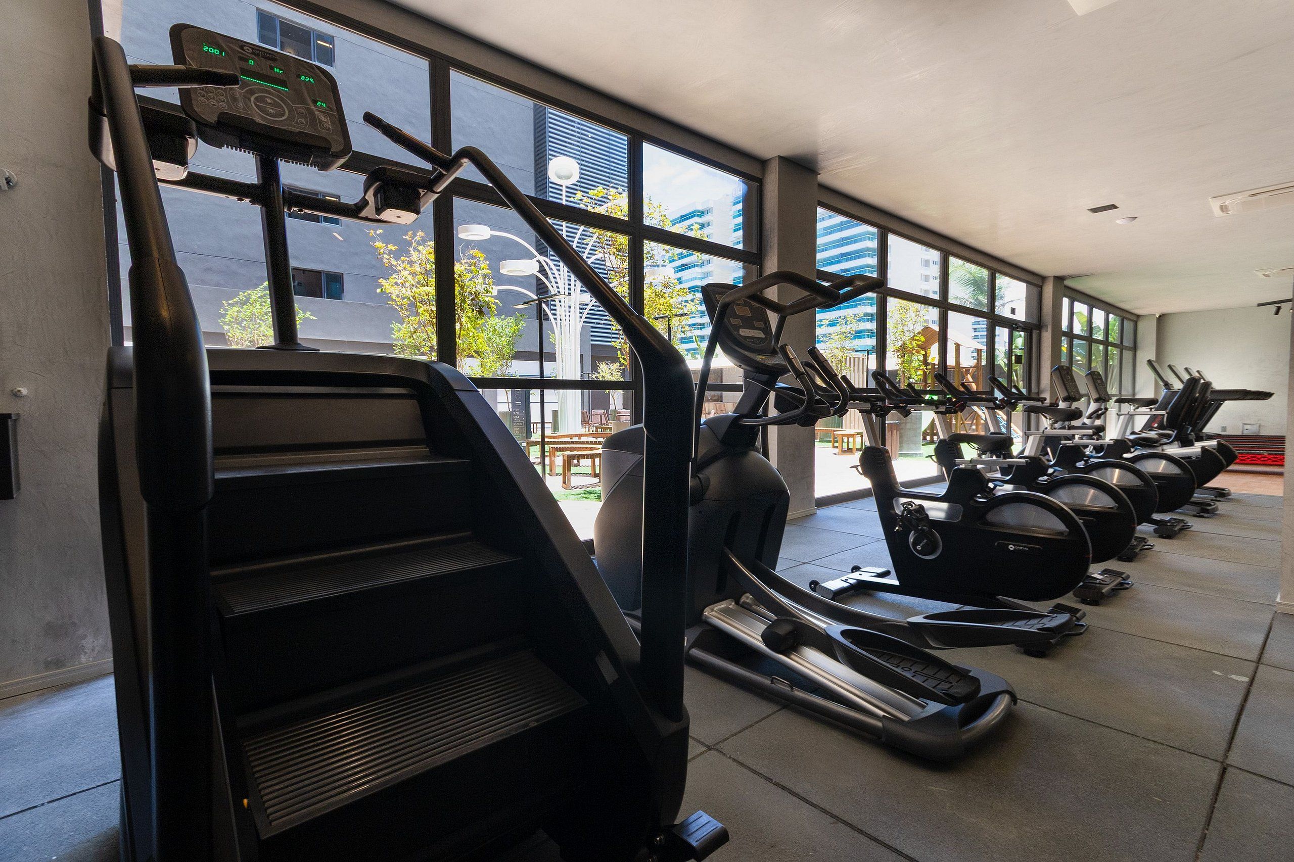Ein Fitnessstudio mit Laufbändern und Crosstrainern, großen Fenstern und Blick auf Gebäude.