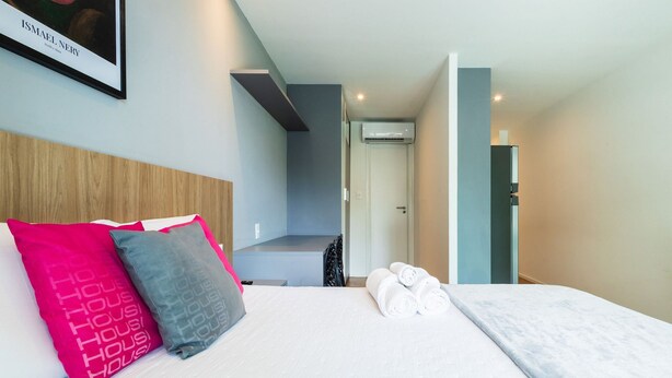 A hotel room with a bed, pillows, a framed picture, and a door leading to another room. - Art Studio Housi Salvador by Carpediem (Salvador)