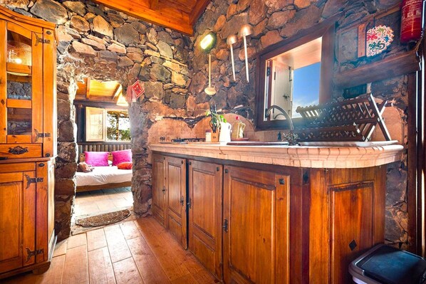 A rustic kitchen with wooden cabinets, a stone wall, and a cozy breakfast nook with a bed. - Holiday Home in Tenerife With Private Garden (Santa Ursula)