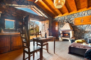 A rustic cabin interior with a stone fireplace, wooden furniture, and a large window overlooking a garden. - Holiday Home in Tenerife With Private Garden (Santa Ursula)