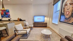 Un salon moderne doté d’un téléviseur à écran plat affichant le logo « NETFLIX », d’un canapé, d’une table basse et d’un coin repas avec un bar.