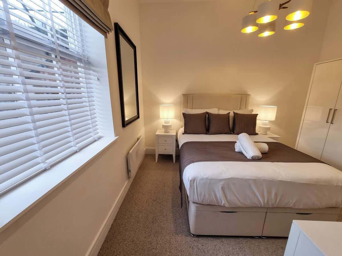 A bedroom with a bed, bedside lamps, a nightstand, a window with blinds, and a wardrobe.