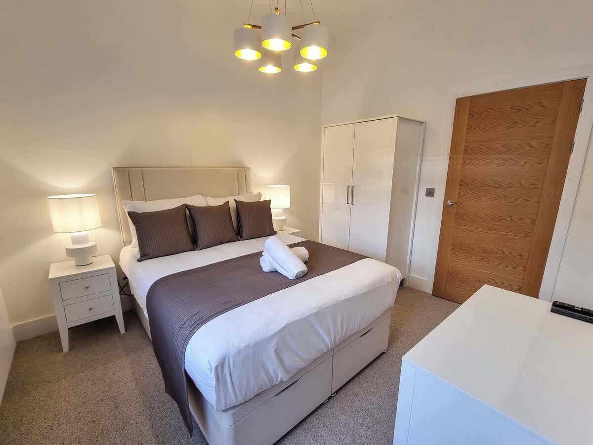 Quarto com cama, mesas de cabeceira, guarda-roupa e luminária no teto.