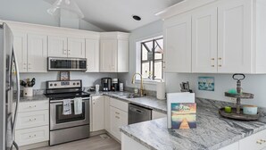 Une cuisine moderne avec des meubles blancs, des appareils en acier inoxydable et un plan de travail en marbre.