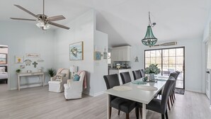 Un vaste espace dédié à la salle à manger, avec une table et des chaises blanches, un ventilateur de plafond et un lustre.