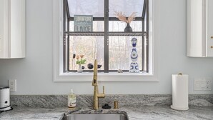 Une cuisine dotée d’un plan de travail en granit, d’un évier en acier inoxydable, d’un robinet doré et d’une fenêtre agrémentée d’objets décoratifs.