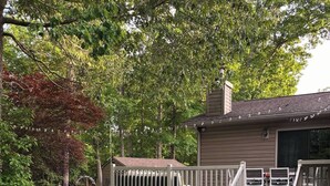 Un bain à remous dans un jardin, avec une terrasse en bois, entouré d’arbres et d’une maison.