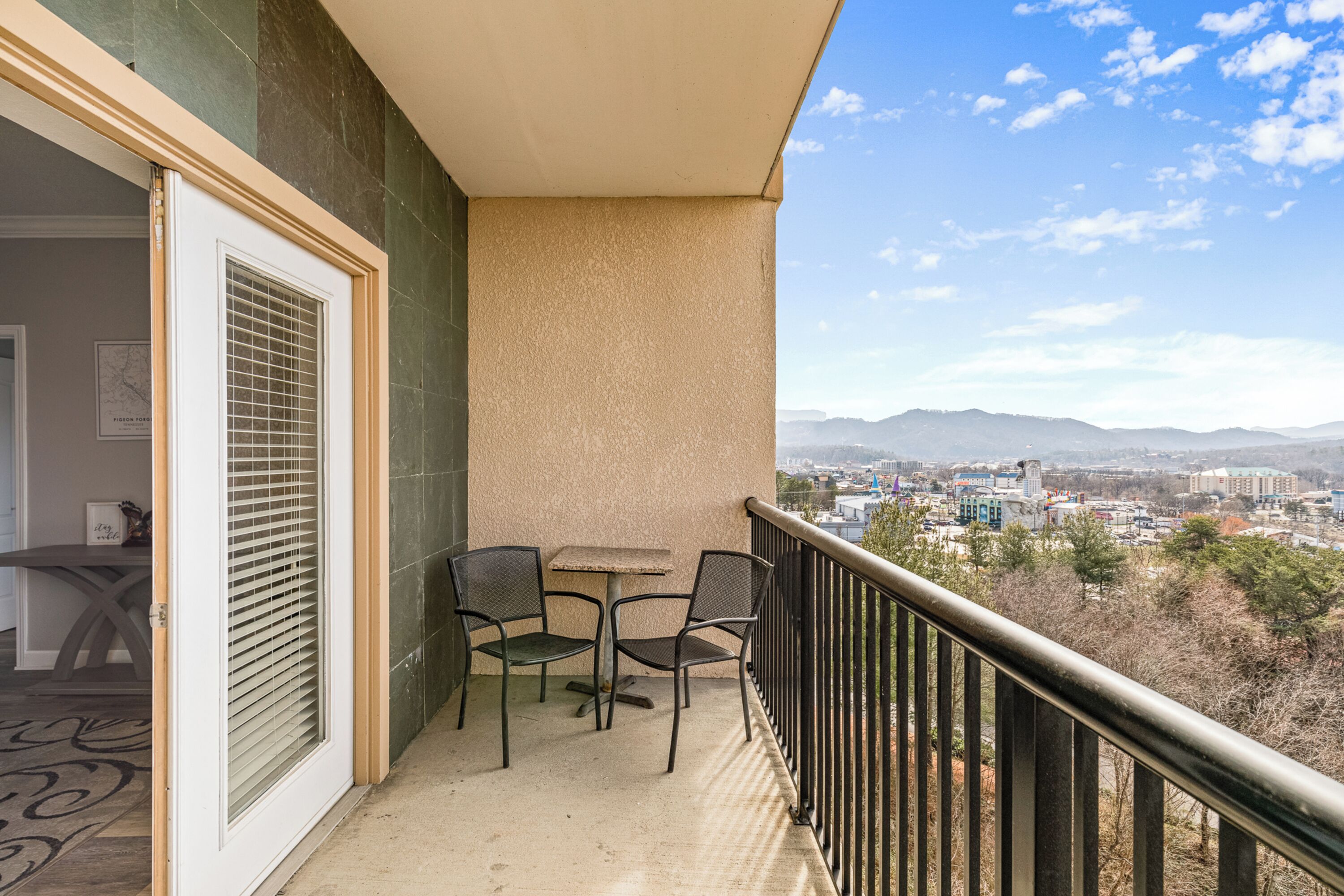 A balcony with a table and chairs, a view of a cityscape and mountains in the distance.