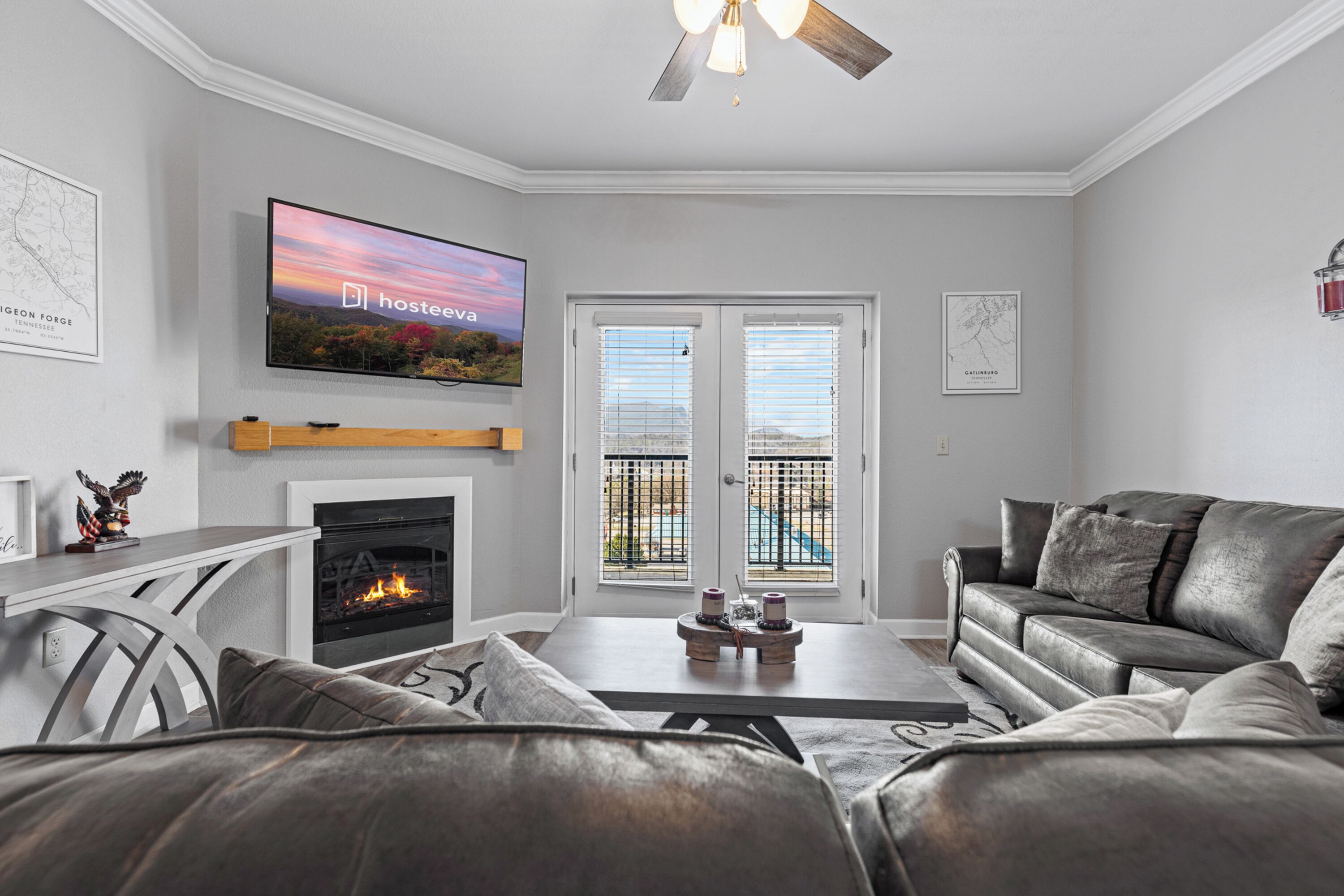A modern living room with a fireplace, leather sofas, a flat-screen TV, and a view through the glass doors.