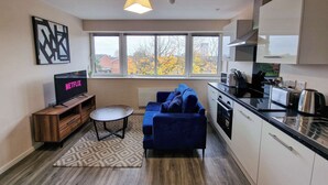 A modern apartment with a kitchen, living area, and a large window with a view of autumn trees. - 1 Bed Media City Flat | Free Parking (Manchester)