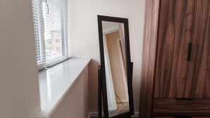 A room with a window, a mirror on a stand, and a wooden wardrobe. - 1 Bed Media City Flat | Free Parking (Manchester)