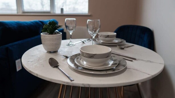 A round dining table with a white marble top, a small potted plant, two wine glasses, a bowl, and cutlery. - 1 Bed Media City Flat | Free Parking (Manchester)