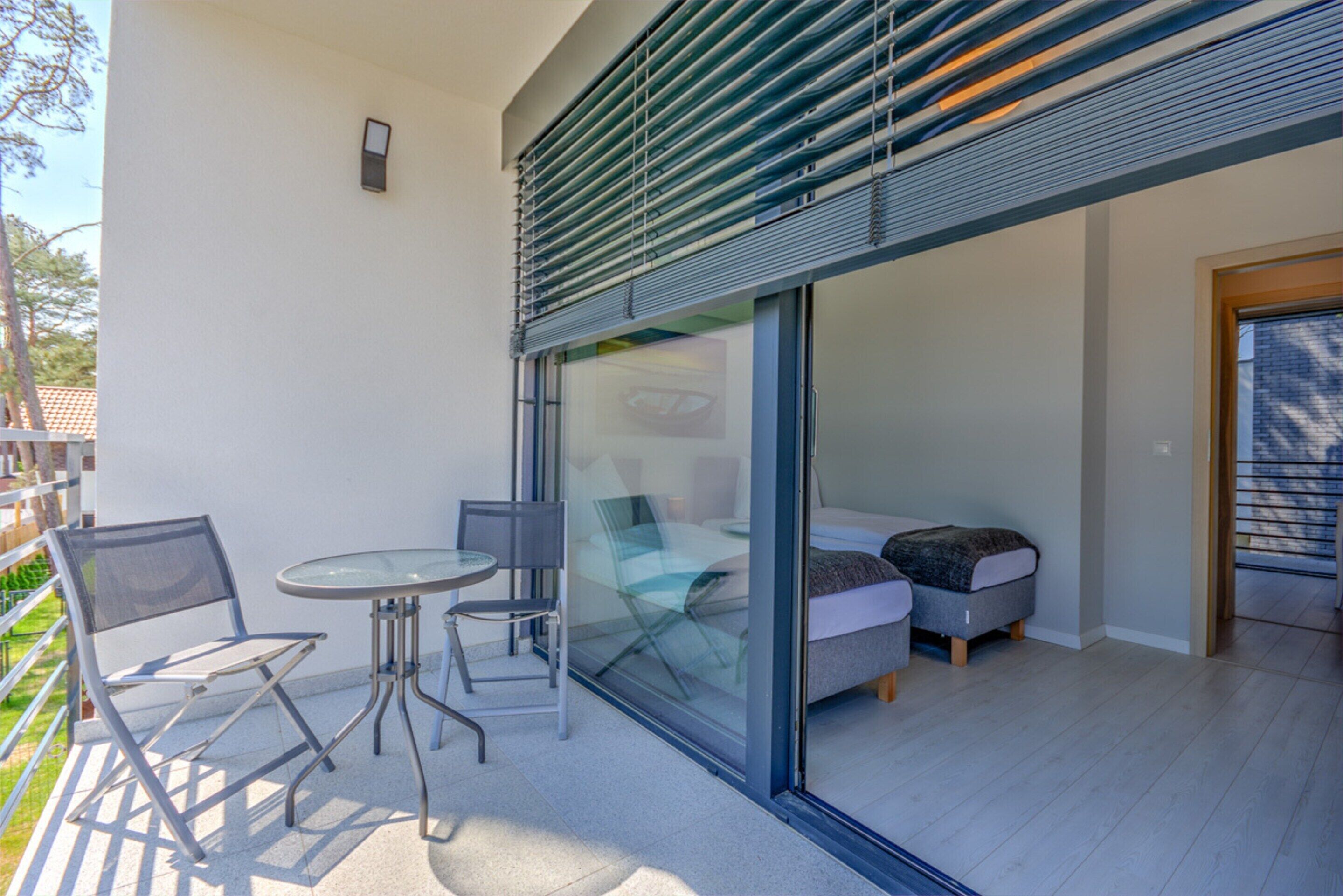 A modern outdoor seating area with a glass partition, a small table, and two chairs.