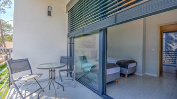 A modern outdoor seating area with a glass partition, a small table, and two chairs.